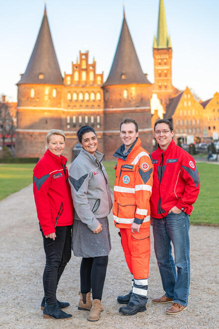 Vier Personen stehen vor dem Holstentor und lächeln in die Kamera.