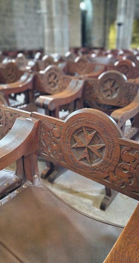 Ein alter Holzstuhl mit einem herausgeschnitztem Johanniter-Kreuz in einer Kirche.