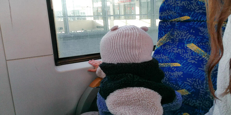 Eine Frau mit einem Kleinkind in einem Linienbus. Das Kind schaut aus dem Fenster.