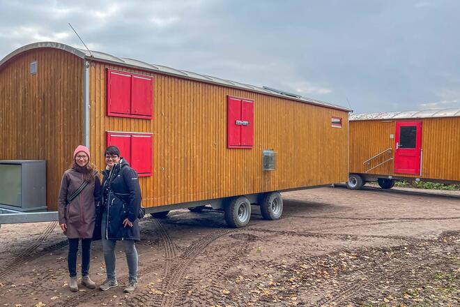 Zwei Mitarbeiterinnen der Johanniter stehen vor dem mobilen Wagen am neuen Standort des Kindergartens.