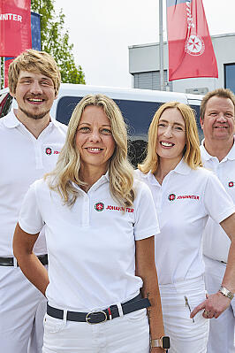 Vier Johanniter stehen vor einem Transporter