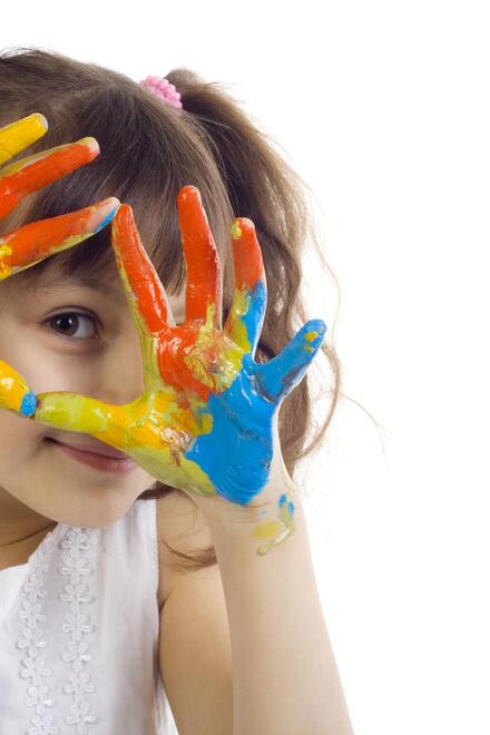 Ein Mädchen schaut lachend durch ihre bunt bemalten Hände, die sie wie einen Rahmen vor ihr Gesicht hält.