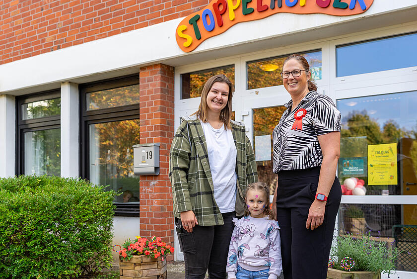 Mutter, Tochter und Erzieherin der Johanniter stehen vor dem Eingang zur Kita Stoppelhopser.