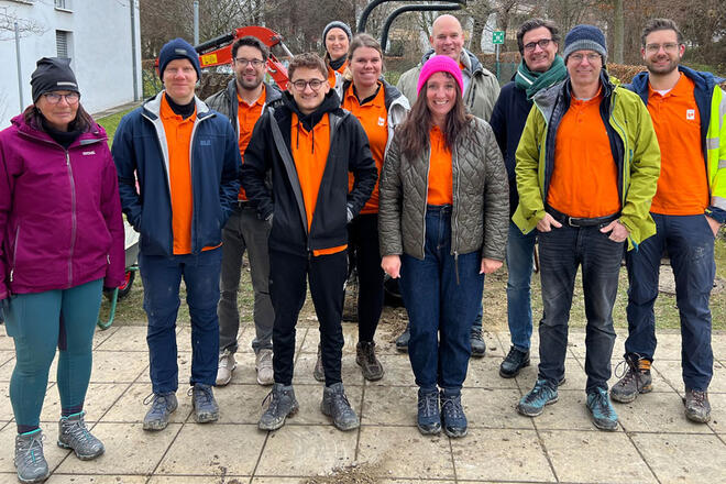 Mehrere Leute in Sixt Dienstkleidung stehen vor einem Garten der von einem Bagger umgegraben wurde.