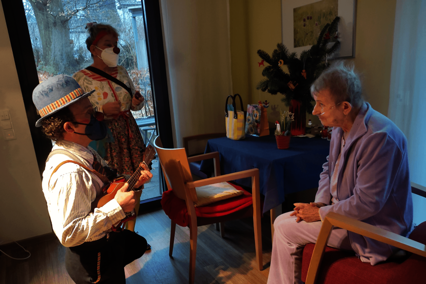 zwei Clowns im Lilge-Simon-Stift stehen und knien vor einer sitzenden Dame.