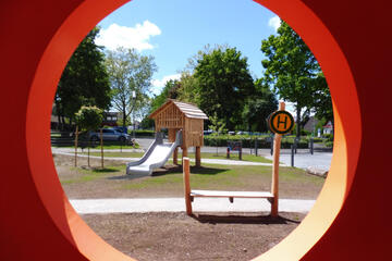 Blick durch ein Spielgerät auf ein Spielhaus