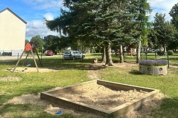 Außenbereich der Kita, mit einem Sandkasten und einer Schaukel im Hintergrund