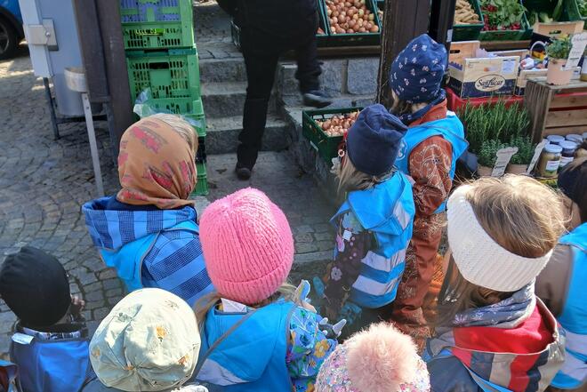 Eine Gruppe von Kindergartenkindern bestaunt die Auslagen auf dem Wochenmarkt.