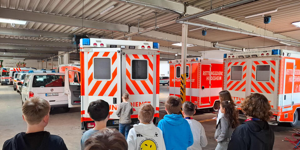 Kinder stehen in einer Fahrzeughalle und schauen auf RTWs