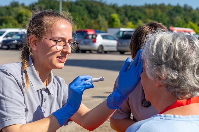 Eine Sanitätshelferin kontrolliert mit einer Diagnostikleuchte die Pupillen einer Patientin.