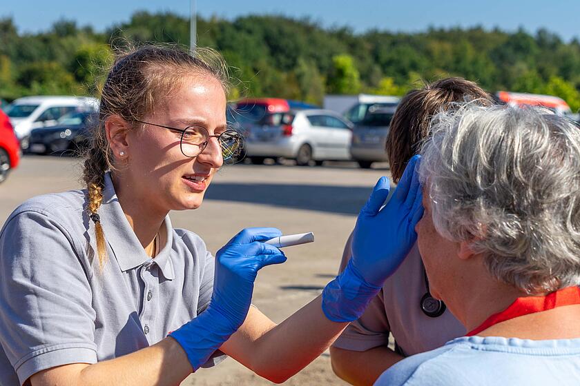 Eine Sanitätshelferin kontrolliert mit einer Diagnostikleuchte die Pupillen einer Patientin.