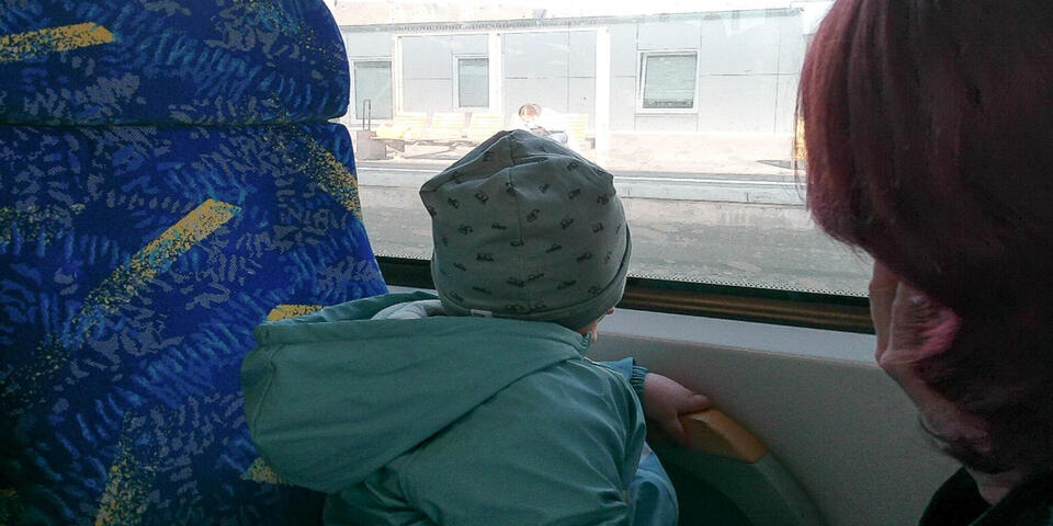 Eine Frau mit einem Kleinkind in einem Linienbus. Das Kind schaut aus dem Fenster.