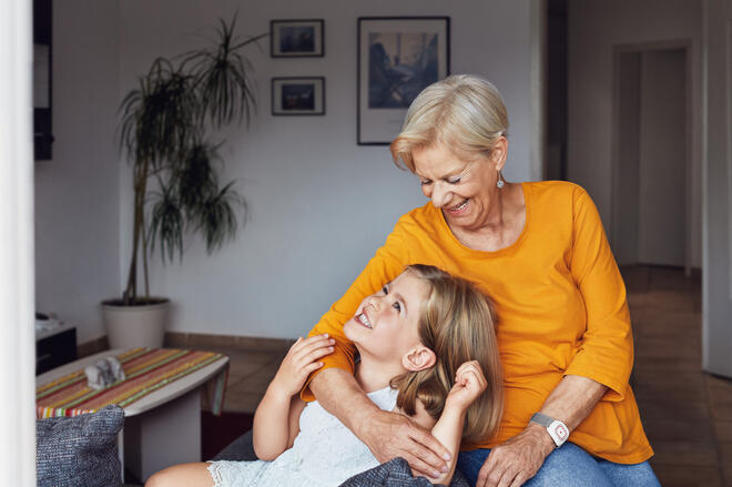 Eine Oma hält ihre Enkelin im Arm. Beide freuen sich.