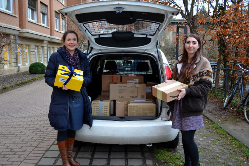 Judith Seiffert, Pressesprecherin des Sankt Bernward Krankenhauses, mit ihrer Kollegin aus der Öffentlichkeitsarbeit. Beide stehen neben einem AUto mit geöffnetem Kofferraum. Darin zu sehen sind zahlreiche Pakete für die Johanniter-Weihnachtstrucker.