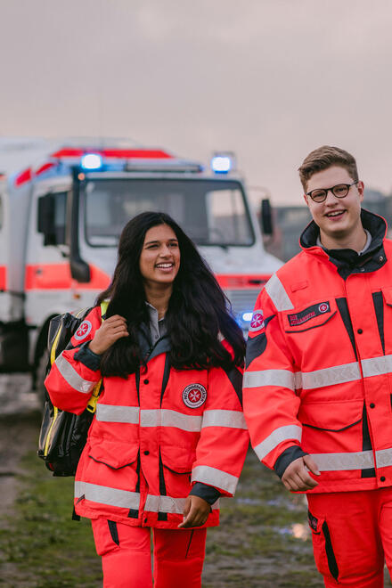 Zwei Personen in Johanniter-Einsatzkleidung stehen vor einem Unimog