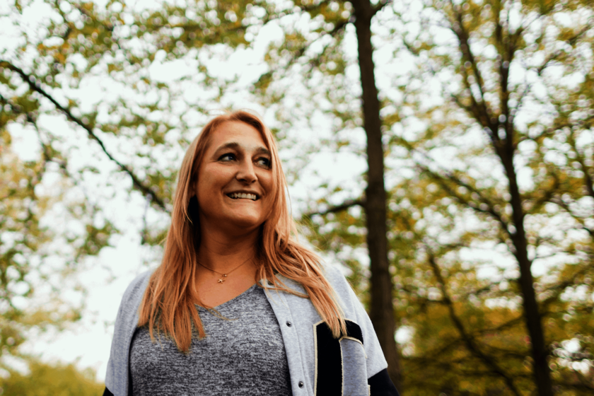 Eine Frau in einer Parkanlage. Sie hat lange rötliche-blonde Haare und blickt seitlich vom Fotografen weg. 