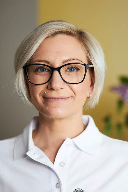 Eine Frau mit Brille steht vor einer gelben Wand