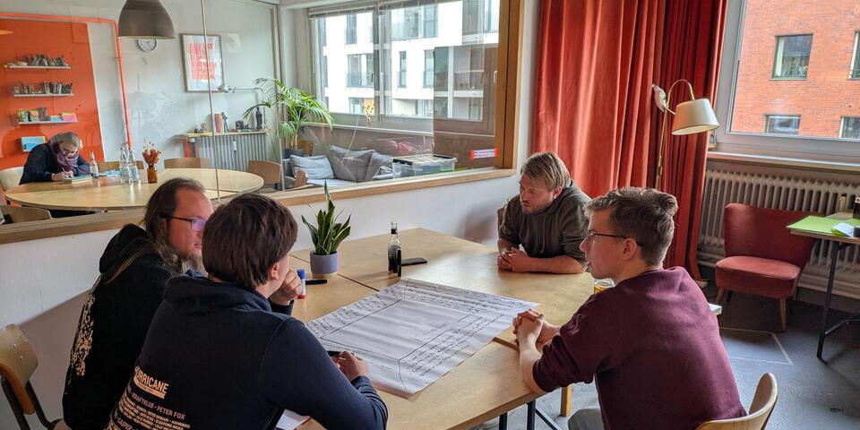 Vier Personen an einem Tisch vor einem großen Papier