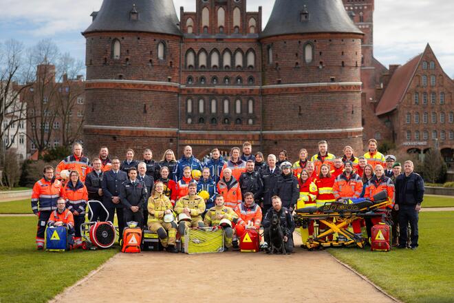 Eine Gruppe von Einsatzkräften der Hilfsorganisationen, Polizei, Feuerwehr und THW steht vor dem Holstentor in Lübeck.