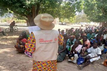 Eine Frau mit Johanniter Weste steht vor einer Gruppe an Menschen und hält einen Vortrag.