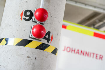 Betonpfeiler mit zwei roten Knöpfen zum öffnen von Garagentoren und schwarz-gelbem Warnband.