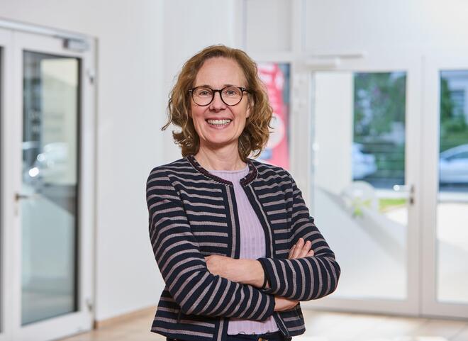 Eine blonde Frau mit Brille und einer gemusterten Strickjacke.