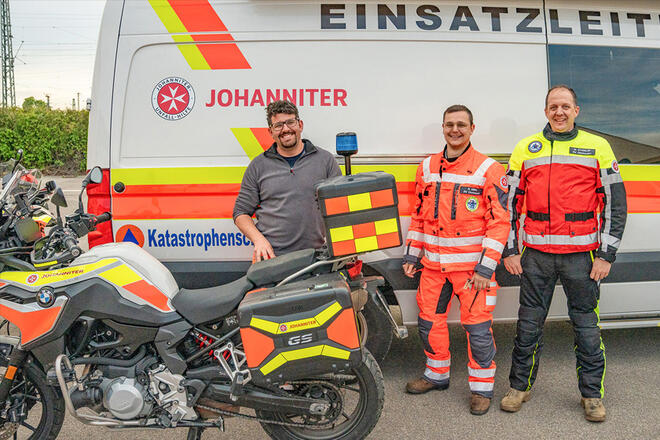 3 Johanniter stehen zwischen verschiedenen Johanniter Einsatzfahrzeugen.