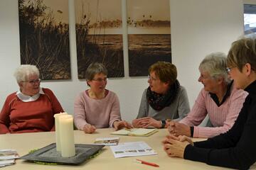 Vier ehrenamtliche sitzen am Tisch mit Kerze und unterhalten sich mit der Koordinatorin.