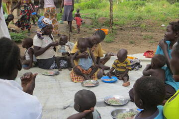 Auf dem Boden sitzende Frauen füttern ihre Kinder mit dem gemeinsam gekochten Essen