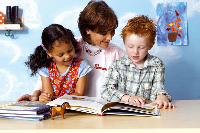 Eine Erzieherin liest zusammen mit zwei Kindern ein Buch