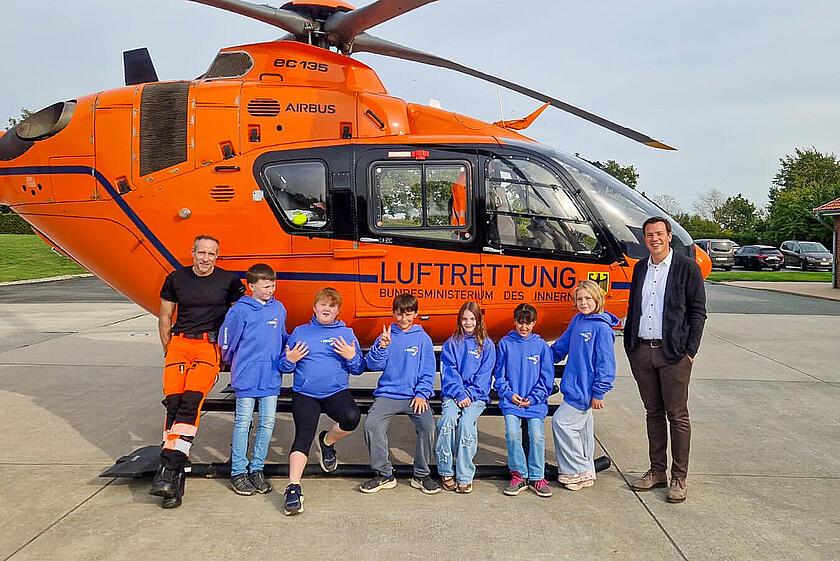 Ein Notfallsanitäter, sechs Kinder und ein Mitglied des Regionalvorstandes stehen vor einem Rettungshubschrauber der Johanniter.