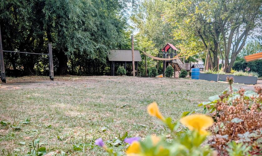 Blick über das Außengelände der Kita Erkrath: Im Vordergrund Blumen, dahinter Wiese, Sandspielbereich und Spielhäuschen