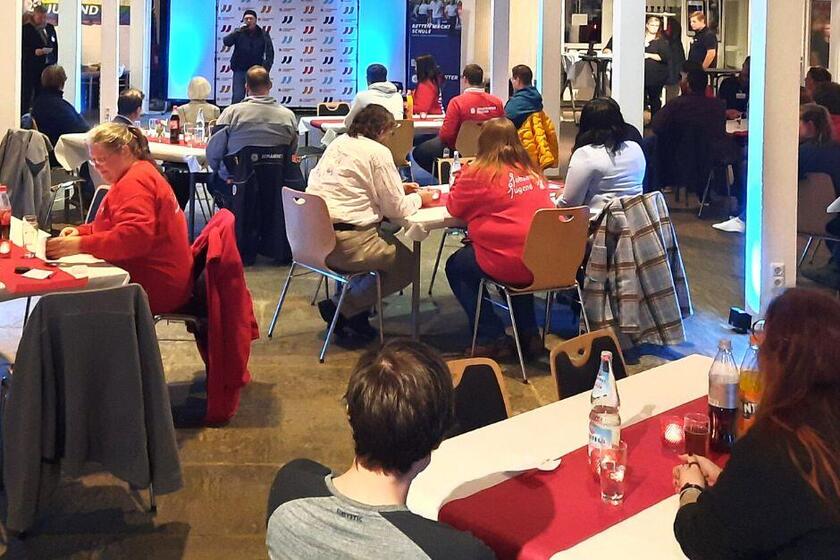 Ein größerer Raum, in dem Gruppentische stehen, die eingedeckt sind. Der Raum ist mit Johanniter-Jugend-Elementen geschmückt und gemütlich beleuchtet.