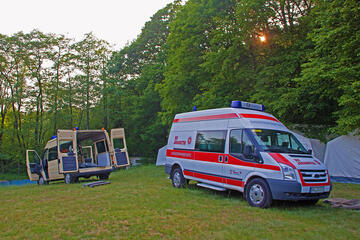 Zwei Johanniterautos stehen auf einer Wiese mit offenem Kofferraum und es wird Zeltmaterial entladen