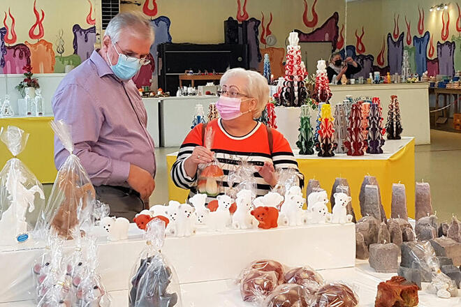 Zwei Teilnehmende schauen sich in der Zierkerzenschnitzerei die zahlreichen Kerzen in allen Formen und Farben an. 