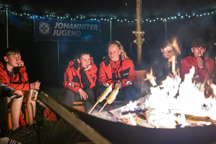 Jugendliche in Johanniter-Jugend-Kleidung sitzen am Lagerfeuer.