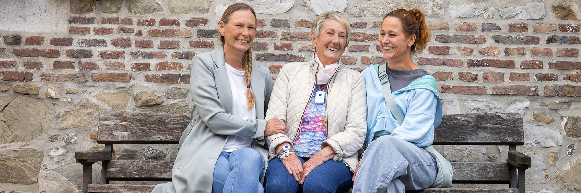 Eine Haunotruf-Kundin sitzt zusammen mit zwei Frauen auf einer Bank vor einem Gebäude.