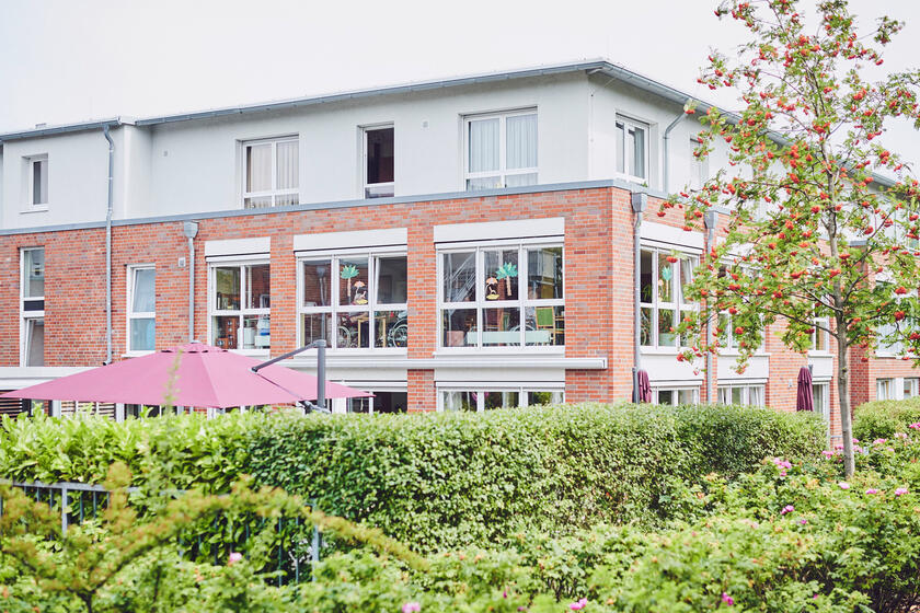 Gebäude hinter Hecke und Gartenanlage