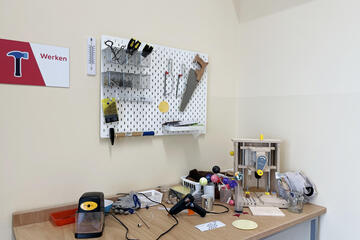 Eine Werkbank mit Bohrer, Kleber, Hammer, Sägen und weiteren Materialien für Kinder.