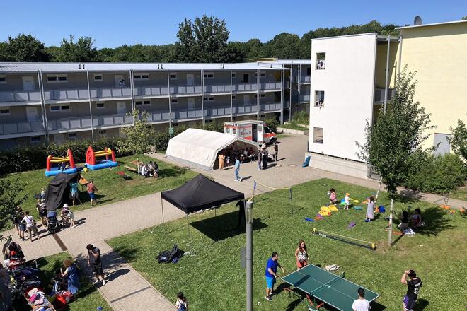 Ein Blick von oben auf einen Innenhof mit Gebäuden, einem Zelt, einem RTW und Menschen