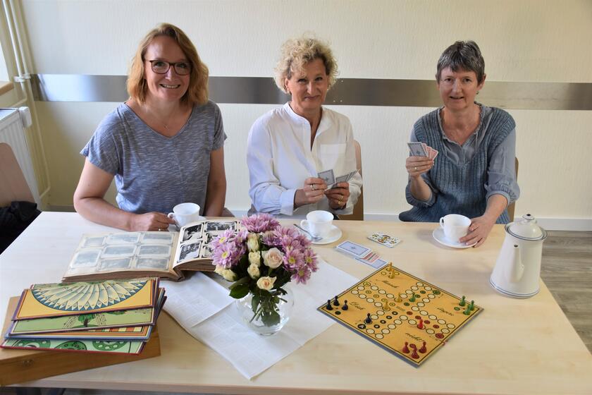 Die Besuchsstunde kann vielfältig genutzt werden: Die Koordinatorinnen Sandra Petersen, Stefanie Lang und Kirsten Wienand von den Johannitern sitzen an einem Tisch, spielen Karten, trinken Kaffee und schauen Fotoalben an.