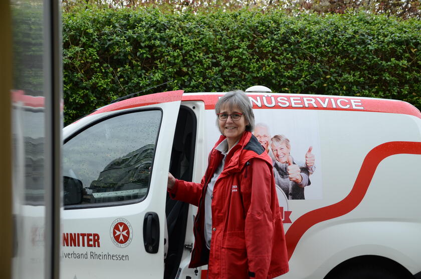 Menüservice Mitarbeiterin vor Fahrzeug