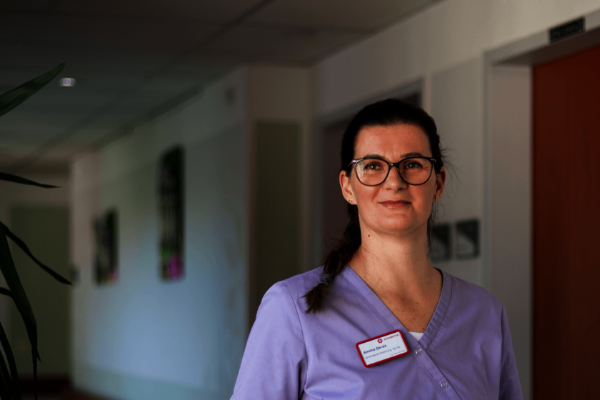 Frau im Flur eines Pflegeheims, trägt Arbeitskleidung und Namensschild.