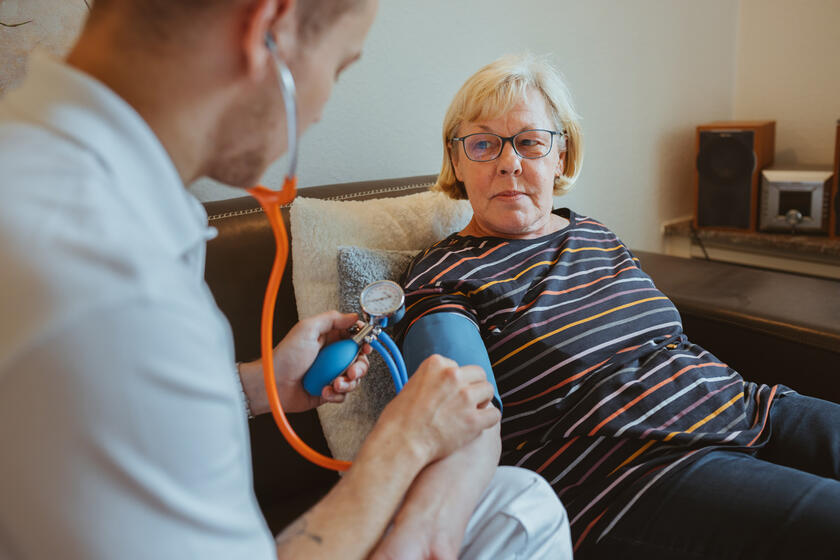 Ambulanter Pflegedienst-Mitarbeiter misst bei einer Seniorin den Blutdruck.