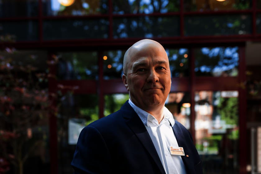 Ein Mann im Anzug steht vor einer Glasfassade mit Namensschild am Revers