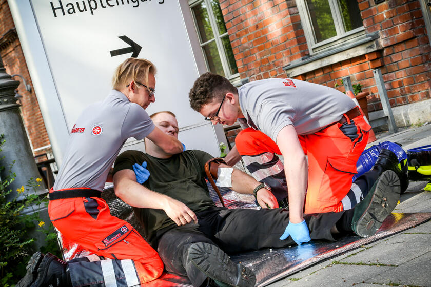 Zwei Johanniter Sanitäter lagern bewusstlosen Mann vor einem Gebäudeeingang.