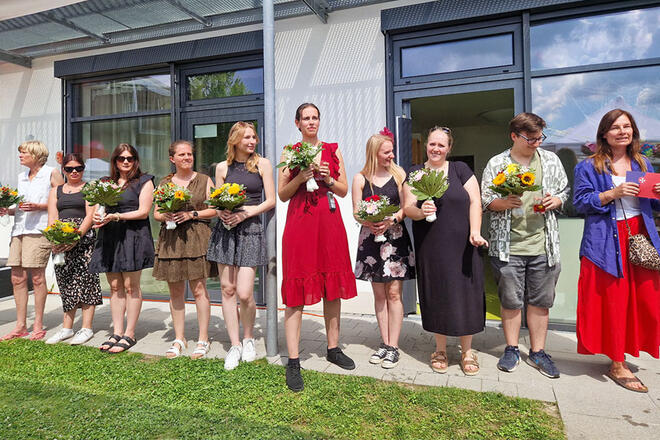 Mehrere Leute stehen vor einem Haus und halten Blumensträußen der Hand.