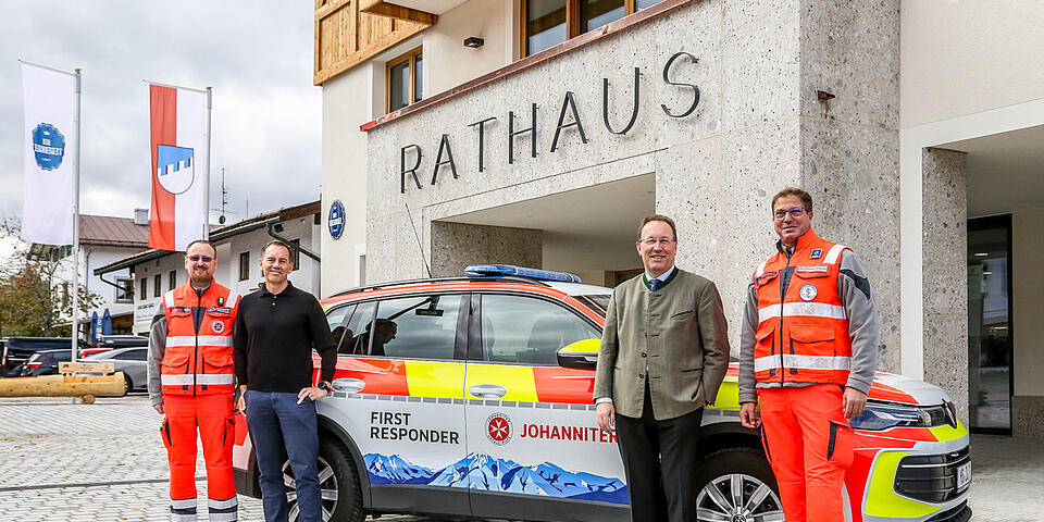 Zwei Bürgermeister und zwei Einsatzkräfte stehen vor neuem Einsatzfahrzeug. Im Hintergrund das Rathausgebäude.