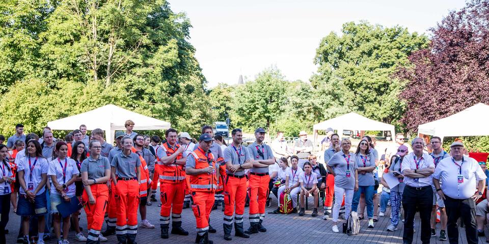  Eine große Gruppe von Einsatzkräften und Helfer*innen im Freien die aufmerksam zuhören