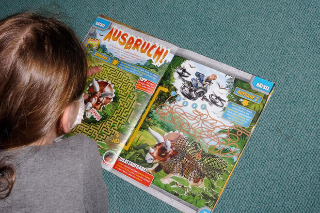 Ein Mädchen aus der Randschulbetreuung blättert in einer Zeitschrift und liegt dabei auf einem Teppich. 